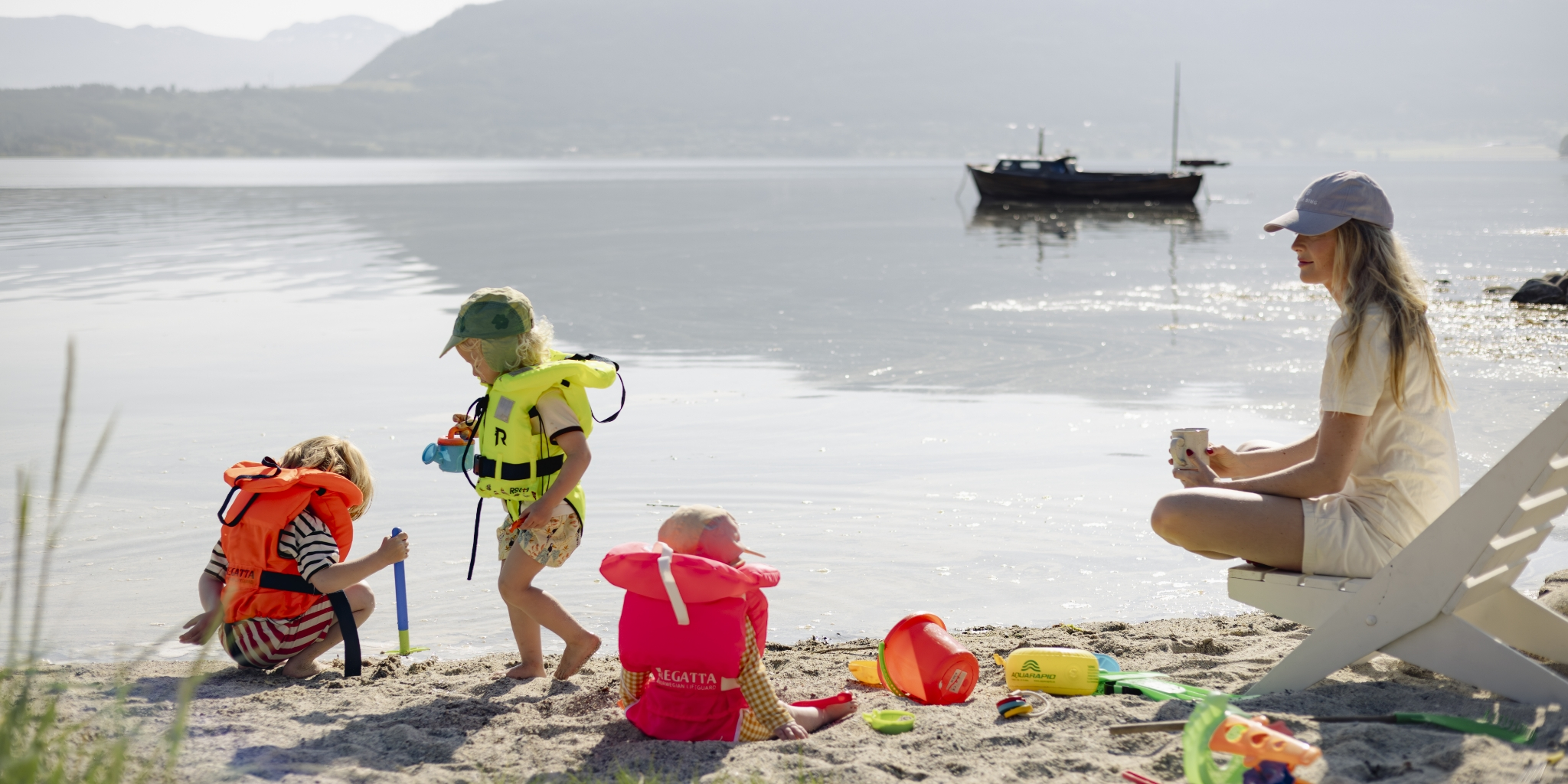 Tre barn leker i vannkanten med redningsvester fra Regatta