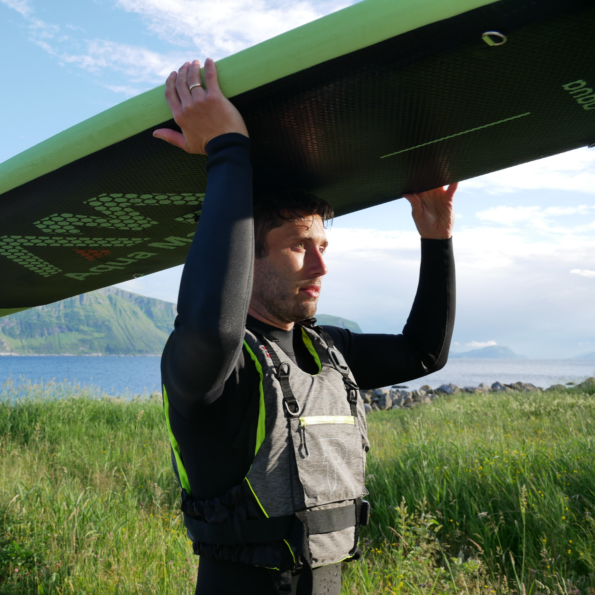 En mann på vei til sjøen for å padle på SUP, iført flytevest fra Regatta